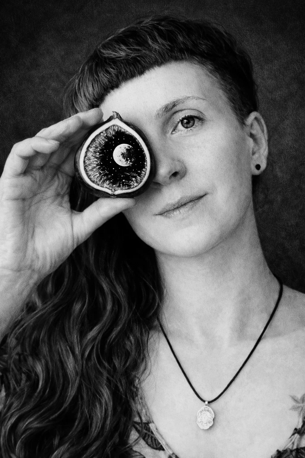 Portrait noir et blanc de l'artiste tenant une figue devant un œil
